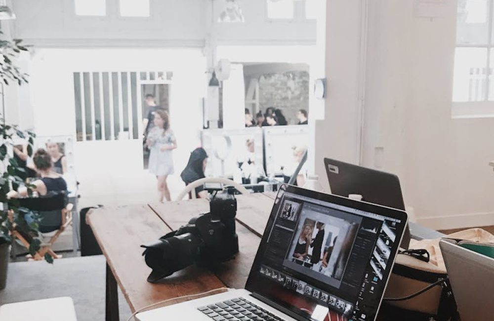 A bright, modern workspace featuring laptops, a camera, and a drawing tablet in an indoor office.